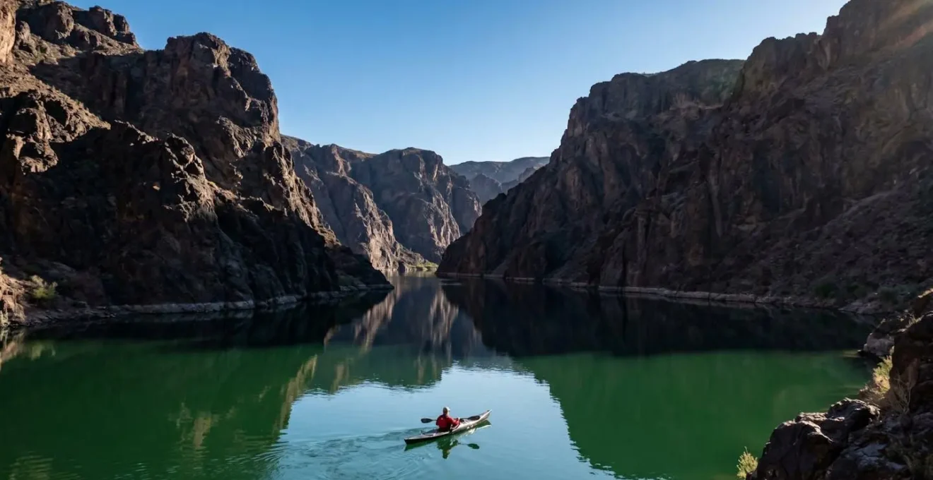 Kayaker paddling through the dramatic Black Canyon on the emerald Colorado River with towering volcanic cliffs