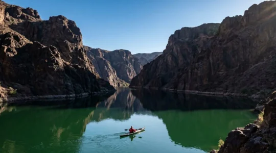 Kayaker paddling through the dramatic Black Canyon on the emerald Colorado River with towering volcanic cliffs