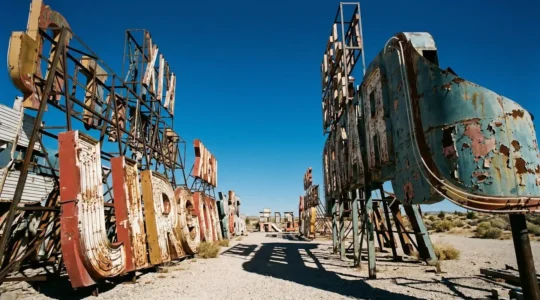 Vintage neon casino signs standing in outdoor desert museum under harsh midday sun with dramatic shadows