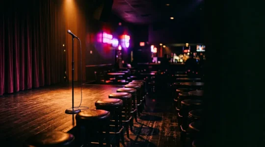 Intimate comedy club stage with warm spotlight and blurred neon lights creating authentic Vegas nightlife atmosphere