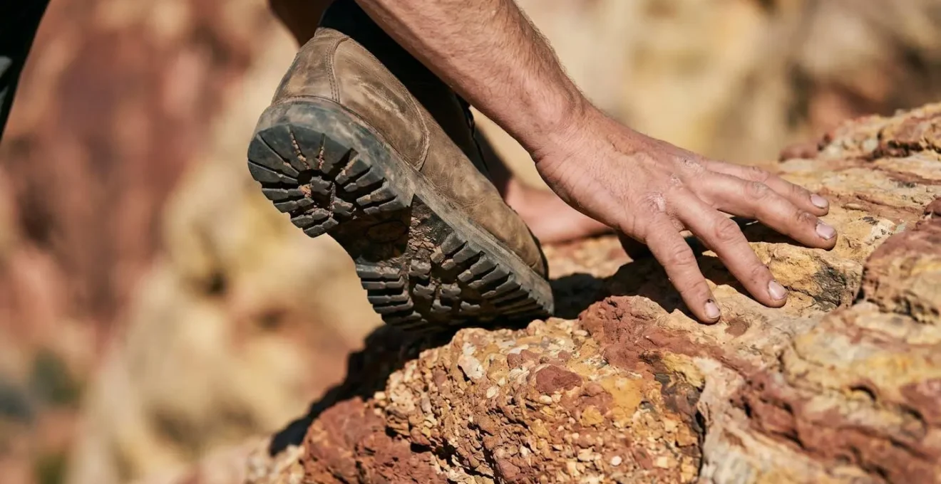 Close-up view of hiking boots and hands navigating textured red sandstone rock scramble illustrating trail difficulty comparison