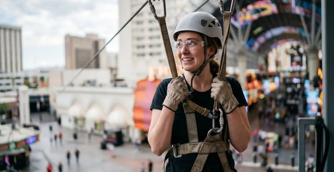 Riders preparing for SlotZilla zipline launch with harness equipment at elevated platform overlooking Fremont Street