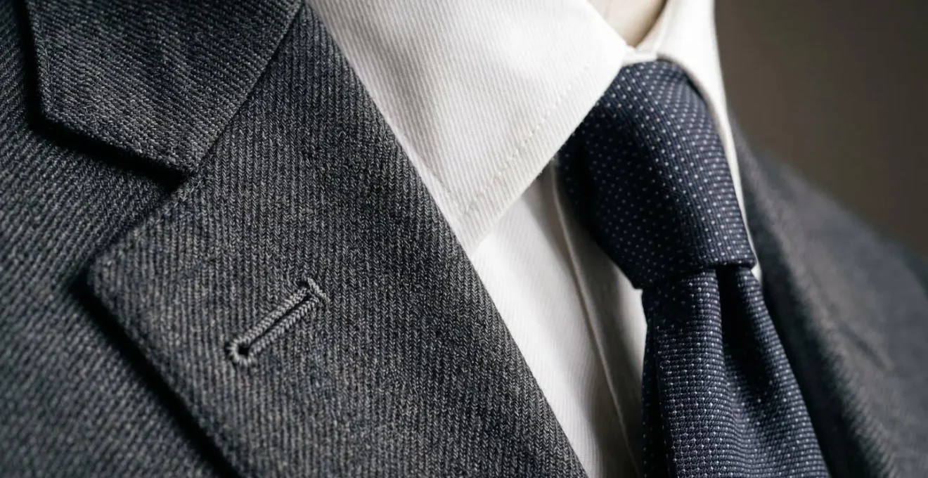 Close-up detail of impeccably tailored 1960s-inspired menswear showing sharp lapel construction and silk tie texture